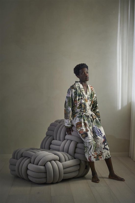 Model zit op een grijze stoel, gekleed in een lichte badjas met veelkleurige jungleprint.