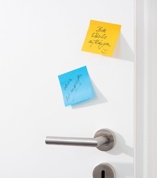 Gele en blauwe Post-it Super Sticky Notes op een witte deur. De gele notitie heeft handgeschreven tekst en een smiley. De blauwe notitie heeft handgeschreven tekst.
