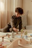 Jongen met donker haar speelt met een houten treinbaan, huisjes en bomen.