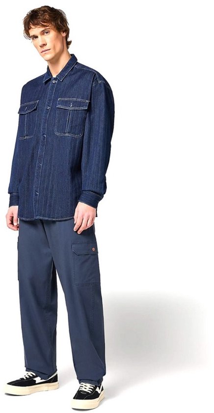 Man in een oversized spijkerhemd en een blauwe cargobroek met twee zakken op de bovenbenen.