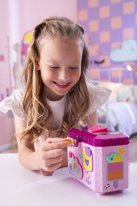Meisje met lang blond haar doet een sticker op een roze glitter sieradendoos. Ze glimlacht en houdt een sticker vast.