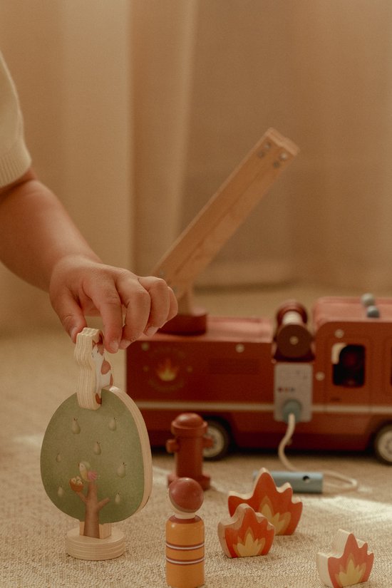 Kind speelt met een houten boom met vogelnestje en houten brandweerwagen accessoires.