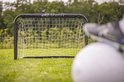 Zwart voetbaldoel met wit net; voetbal en schoen op groen gras