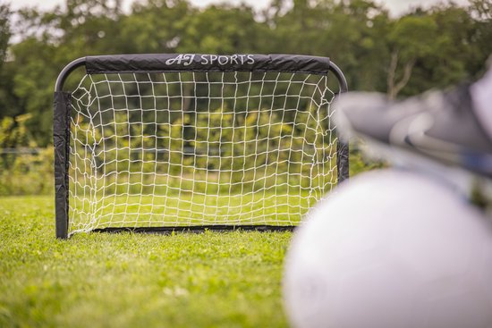 Zwart voetbaldoel met wit net; voetbal en schoen op groen gras