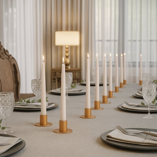 Lange eettafel met een grijze linnen look tafelkleed, gedekt voor een diner met elf witte kaarsen in gouden houders.