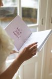Een bruid in witte jurk houdt een open ringband-planner vast met een paarse pagina.
