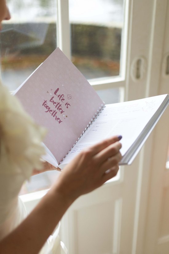 Een bruid in witte jurk houdt een open ringband-planner vast met een paarse pagina.
