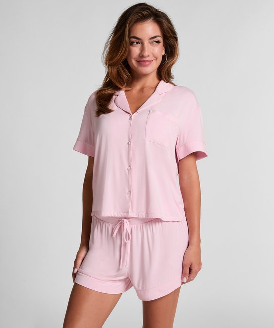 Model draagt een roze pyjamashirt en short. Het shirt heeft korte mouwen en knoopjes. De short heeft een tunnelkoord.