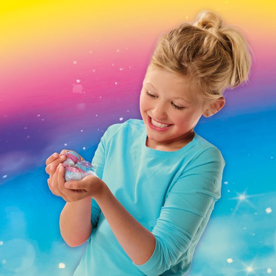 Een lachend meisje met een blauw shirt houdt kleine, roze en blauwe badbruisballetjes vast in haar handen.