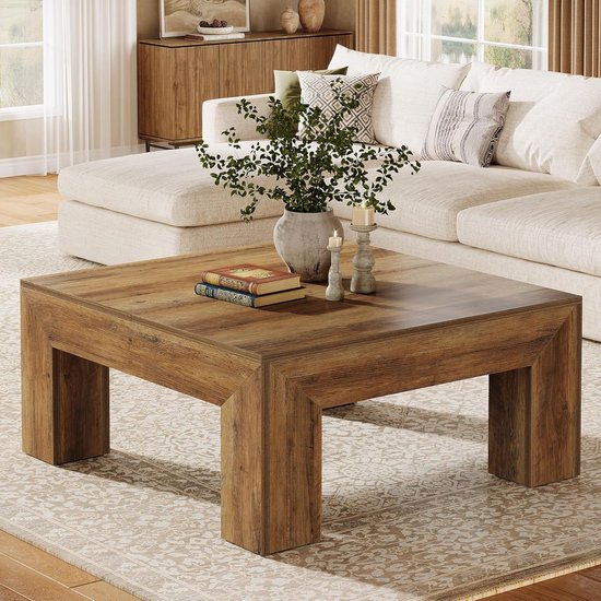 Table basse carrée aspect bois, sur un tapis, avec un canapé et décoration sur la table.