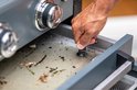 Hand drukt een zwarte knop in, in een grijze lade onder de barbecue.