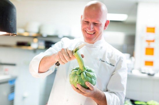 Chef met witte jas snijdt artisjokken in een keuken.