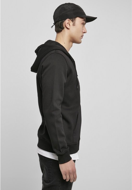 Man met pet, opzij gezien, draagt een effen zwarte hoodie met ritssluiting.