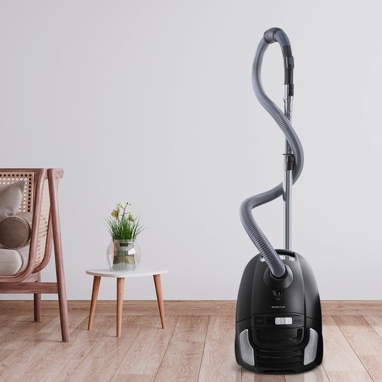 Zwarte stofzuiger met grijze slang en stang, staand op een houten vloer in een woonkamer.