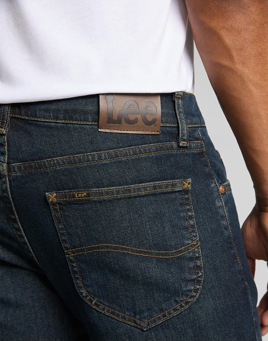 Detail van de achterkant van de donkerblauwe Lee jeans met bruine merkpatch en geborduurde 'Lazy S' stiksels.
