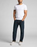 Man met tatoeage in een witte t-shirt en donkerblauwe Lee jeans met omgeslagen pijpen.