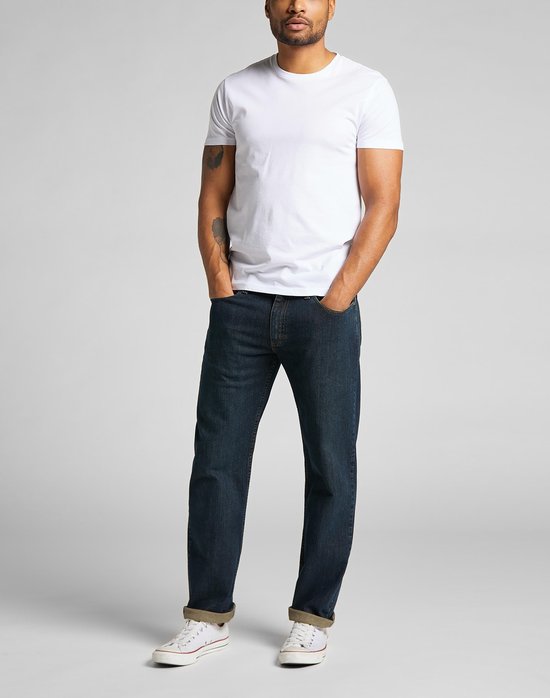 Man met tatoeage in een witte t-shirt en donkerblauwe Lee jeans met omgeslagen pijpen.