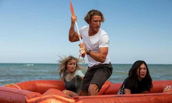 Drie mensen in een oranje reddingsvlot op zee. Een man in het midden houdt een peddel omhoog.