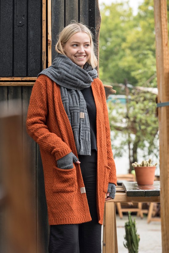 Model draagt lang oranje gebreid vest met grijze sjaal en handschoenen, met zwarte top.