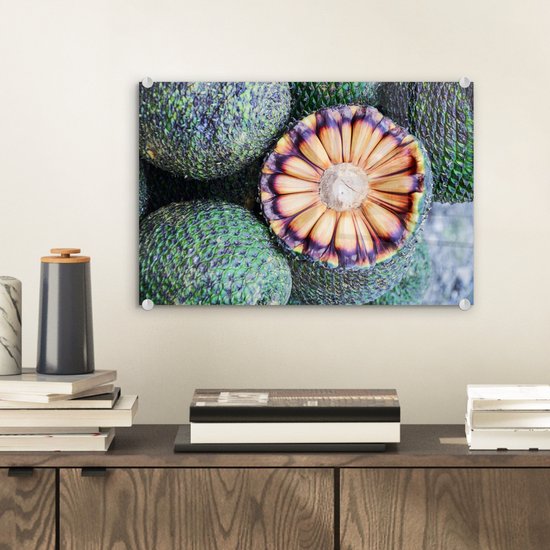 Close-up van een doorgesneden Braziliaans fruit met oranje binnenkant en groene schubben. De schilderij hangt aan een witte muur.