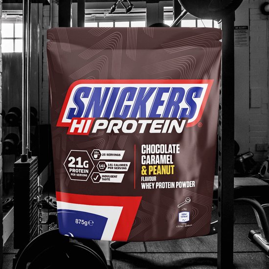 Snickers Hi Protein poeder in chocolade-, karamel- en pindasmaak, in een fitnessruimte. Bruine zak met rode en witte details. 21g eiwit per portie.
