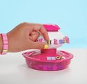 Hand met roze armbandjes gebruikt de Pop Style armbandjesmaker, met roze en paarse onderdelen.