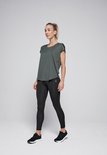 Vrouw draagt donkergroen shirt en zwarte legging, staat met haar gezicht naar de zijkant, kijkend weg.