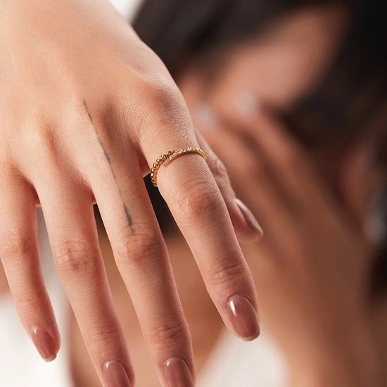 Gouden klemring met zirkonia en bubbels aan de uiteinden, gedragen door een vrouw.