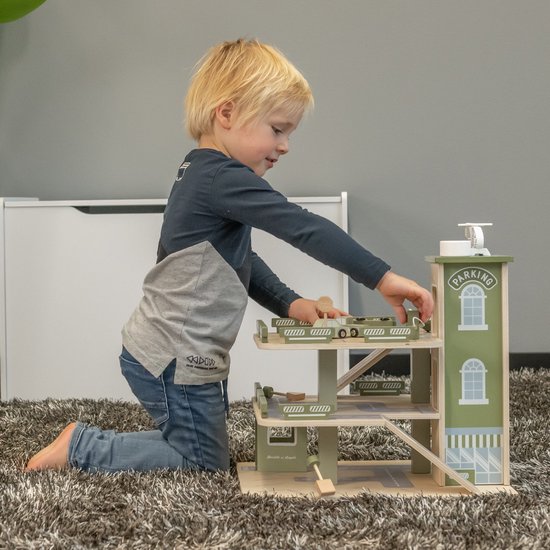 Jongen met blonde krullen speelt met de houten speelgoedparkeergarage in retro groen.