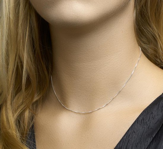 Een dunne zilverkleurige Venetiaanse schakelketting van 38 cm, gedragen om de nek van een vrouw.