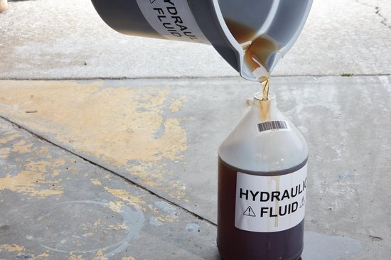 Motorolie wordt gegoten uit een jerrycan in een fles met een label "HYDRAULIC FLUID".