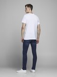 Model in een wit T-shirt, kijkend weg, met blauwe spijkerbroek.