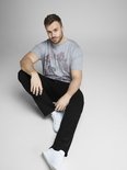 Man met een grijze T-shirt met bloemenprint en zwarte jeans, zittend.