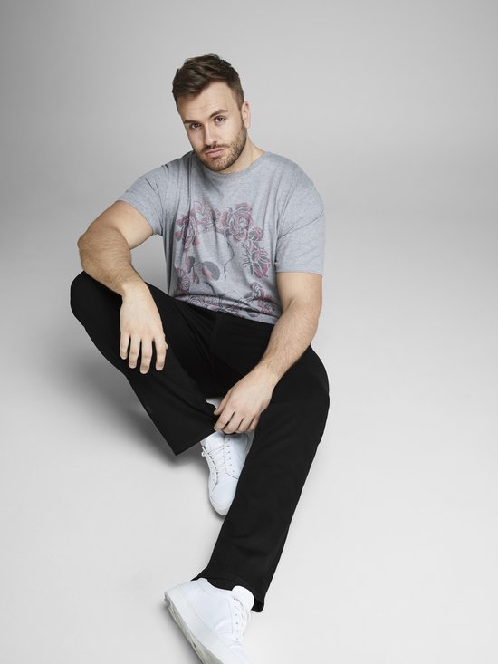 Man met een grijze T-shirt met bloemenprint en zwarte jeans, zittend.