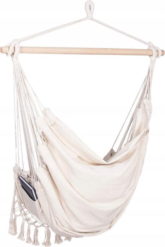 Witte hangstoel met macramé, franjes, kussens en boekenvak. Houten spreider.