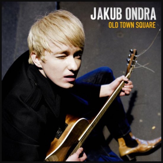 Jonge man met blond haar, knipoogend, met akoestische gitaar. Titel: 'JAKUB ONDRA OLD TOWN SQUARE'.
