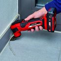 Een hand houdt een rode en zwarte multitool met accu vast om voegsel te verwijderen bij een tegelmuur.