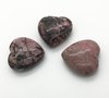 Drie roze rhodoniet hartjes met zwarte aders op een witte achtergrond.