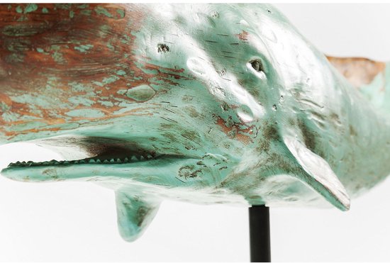Close-up van een verweerd turquoise en bruin houten walvisbeeld, met een open mond en tanden, op een zwarte standaard.