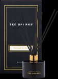 Zwarte glazen diffuser van Ted Sparks met gouden dop en zwarte stokjes, naast de verpakking.
