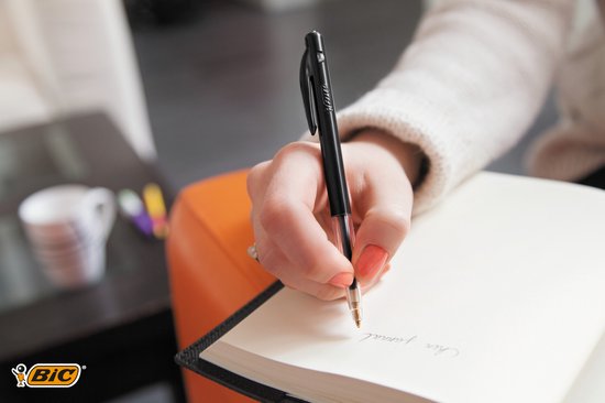 Hand met een zwarte BIC balpen die schrijft in een notitieboek.