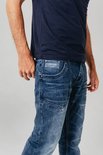 Man in een blauwe jeans met stone wash used look. Gedetailleerde zakken op de voorkant.