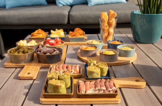 Buiten op een houten tafel staan hapjes in schaaltjes op serveerplanken