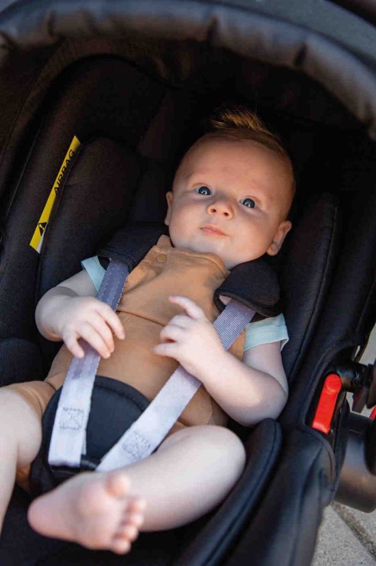 Baby met blauwe ogen en ondeugend kapsel zit in een zwart autostoeltje.