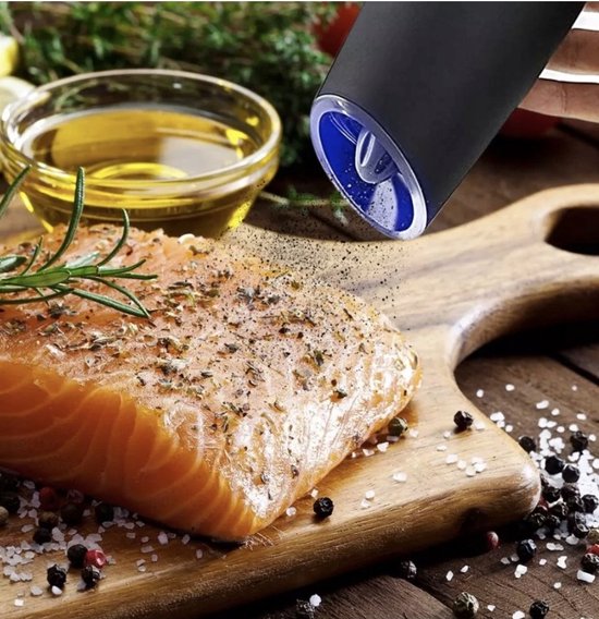 Elektrische pepermolen maalt zwarte peper op een stuk zalm op een houten snijplank.