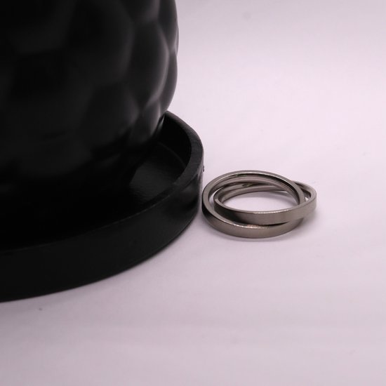 Twee zilverkleurige ringen in elkaar, naast een zwarte vaas op een witte ondergrond.