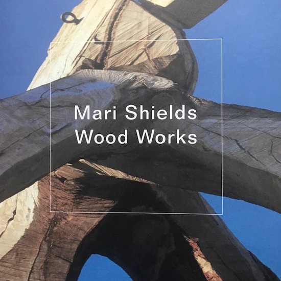 Boek "Mari Shields Wood Works", met een close-up van houtsnijwerk tegen een blauwe lucht.