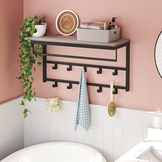 Grijze houten kapstok met zwart metalen frame in een badkamer. Een handdoek, sponS en borstel hangen aan de haken. Planten, zeep en handdoeken op de plank.
