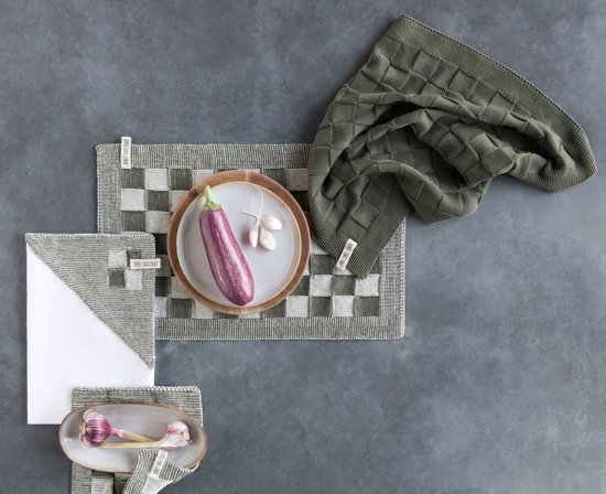Diverse gebreide items op een grijze ondergrond: een aubergine, knoflook, en keukentextiel met blokjespatroon en huizenpatroon.
