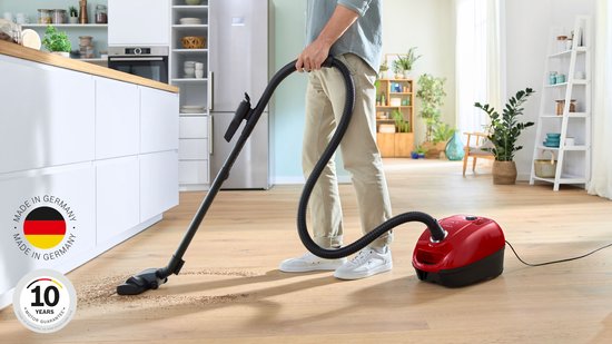 Man stofzuigt een houten vloer met rode Bosch stofzuiger. Logo "Made in Germany" en "10 Years Motor Guarantee".